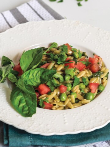 Pesto orzo in a skillet with wooden spoon and topped with tomatoes