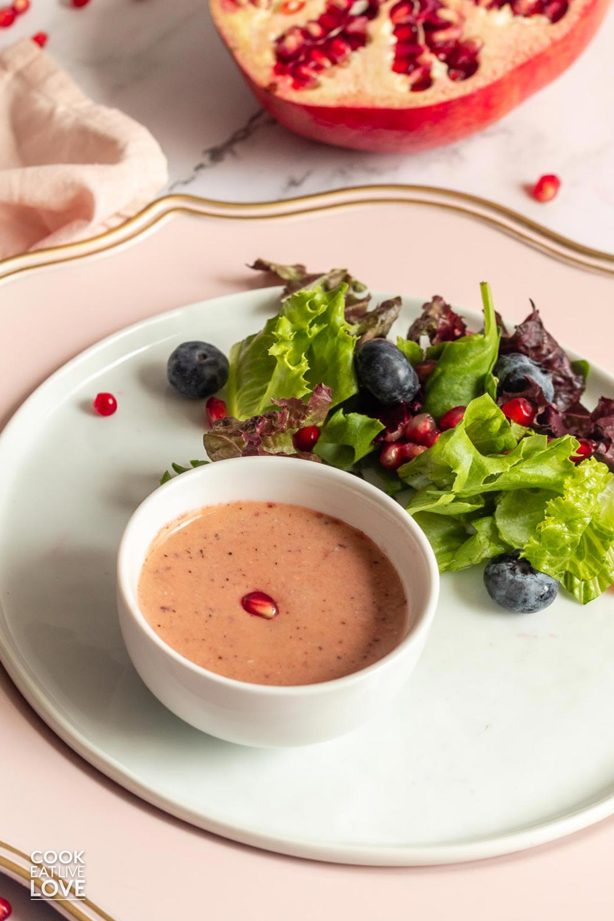 Pomegranate dressing in a little bowl on a plate with some salad.