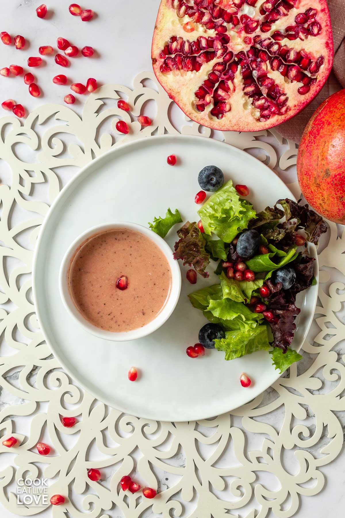 Pomegranate dressing on a plate with salad and a half a pomegranate on the table.