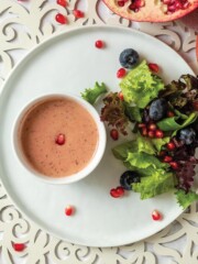 Pomegranate vinaigrette on concrete counter top with wooden spoon surrounded by pomegranate arils.