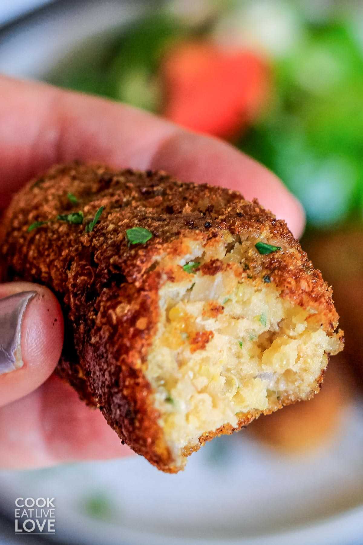 A hand holding a vegetarian croquette up with a bite missing.