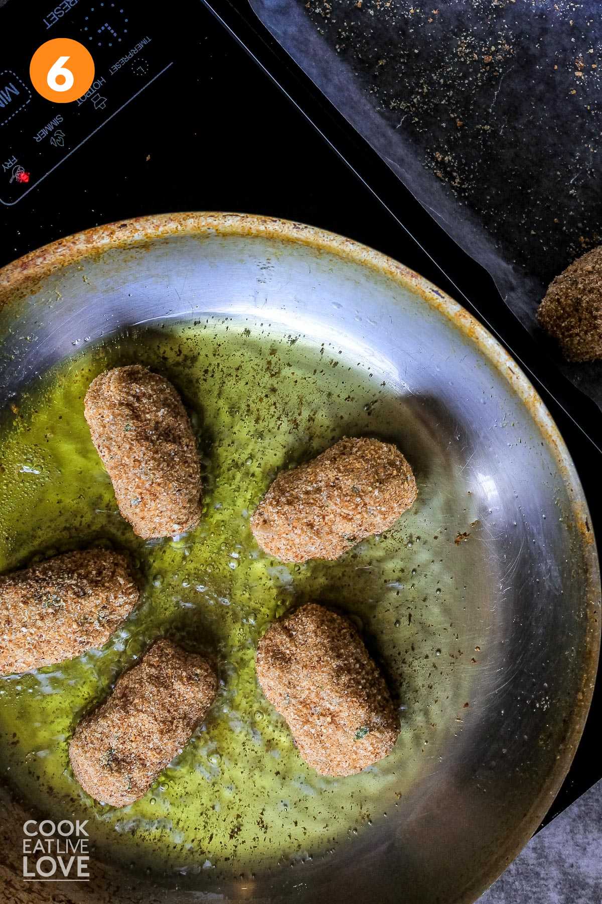 Overhead view of breaded croquettes cooking in pan with oil.