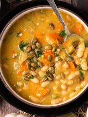 Pumpkin white bean soup in a bowl with a spoon in it.