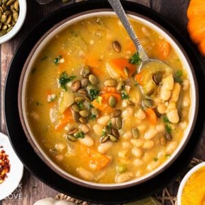 Pumpkin white bean soup in a bowl with a spoon in it.