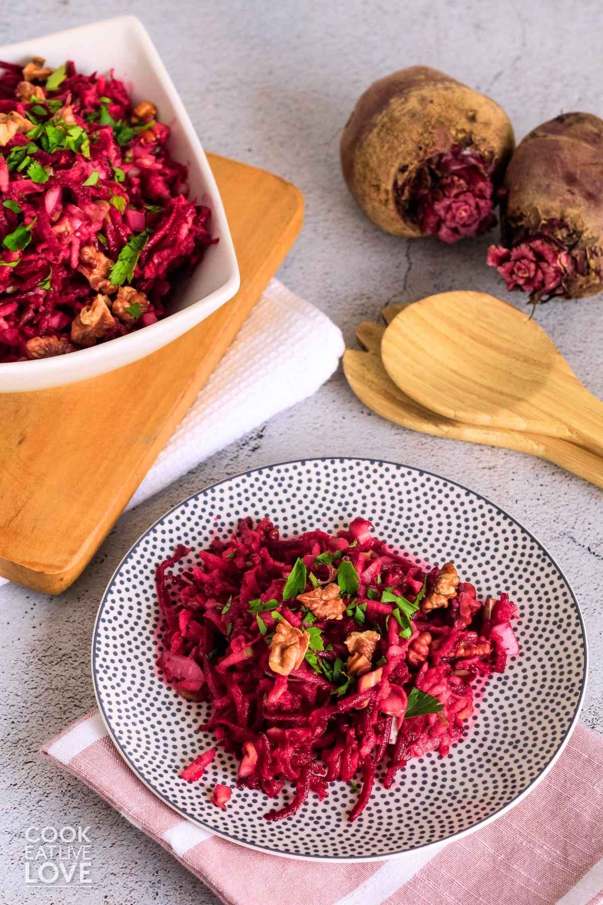 Raw beet salad on a gray polka dot plate with a pink and white napkin and serving spoons to the side.