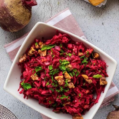Closeup view of beetroot and apple salad on plate with serving bowl in background.