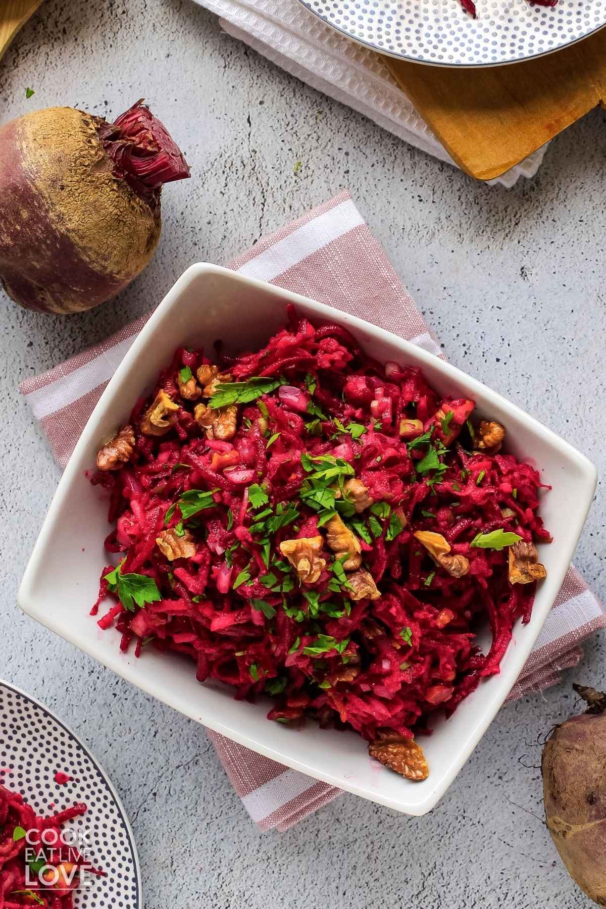 Beet and apple salad in a square bowl on the table with whole fresh beets to the side.