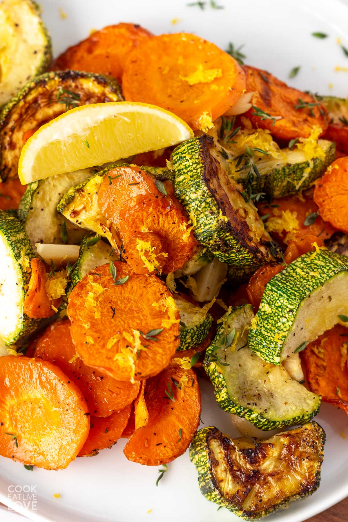 Roasted carrots and zucchini with lemon zest on top and a lemon wedge.