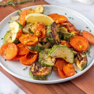 A plate of roasted zucchini and carrots on the table with a lemon wedge.