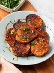 A plate of balsamic miso roasted sliced sweet potatoes garnished with parsley.