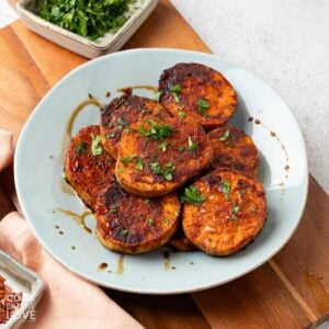 A plate of balsamic miso roasted sliced sweet potatoes garnished with parsley.