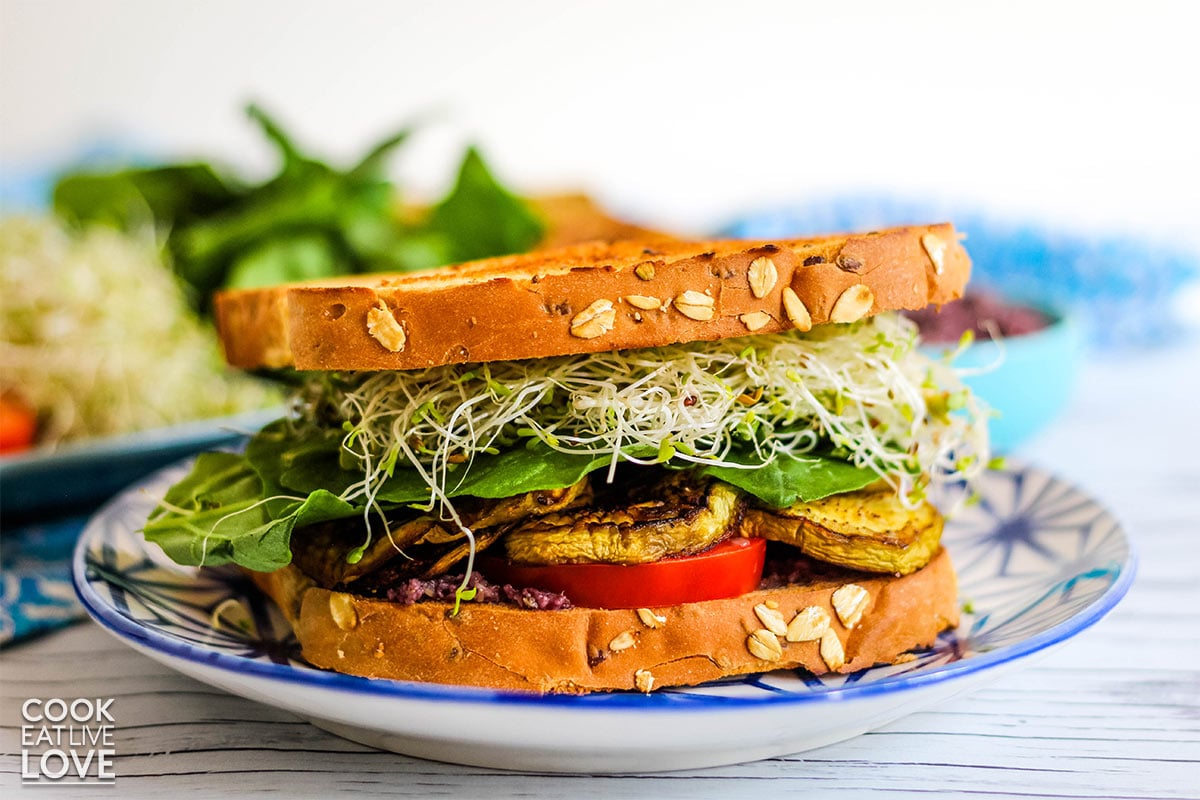 Sandwich on blue plate with sprouts, greens and veggies