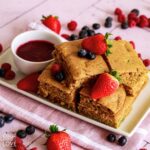 Sheet pan pancakes on a white platter with berries.