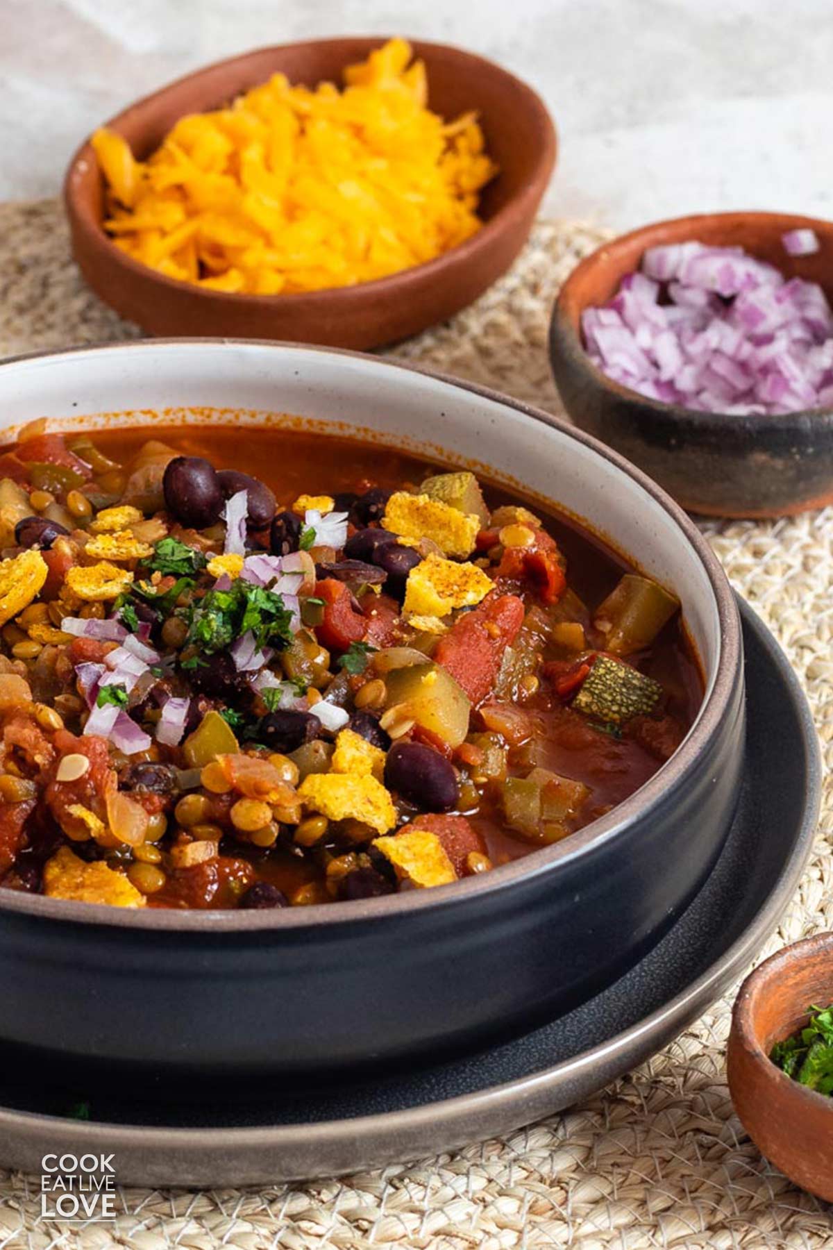 A bowl of vegetarian chili with beans and lentils on the table with cheese and red onion.
