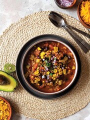 A bowl of vegetarian bean chili on the table with toppings.