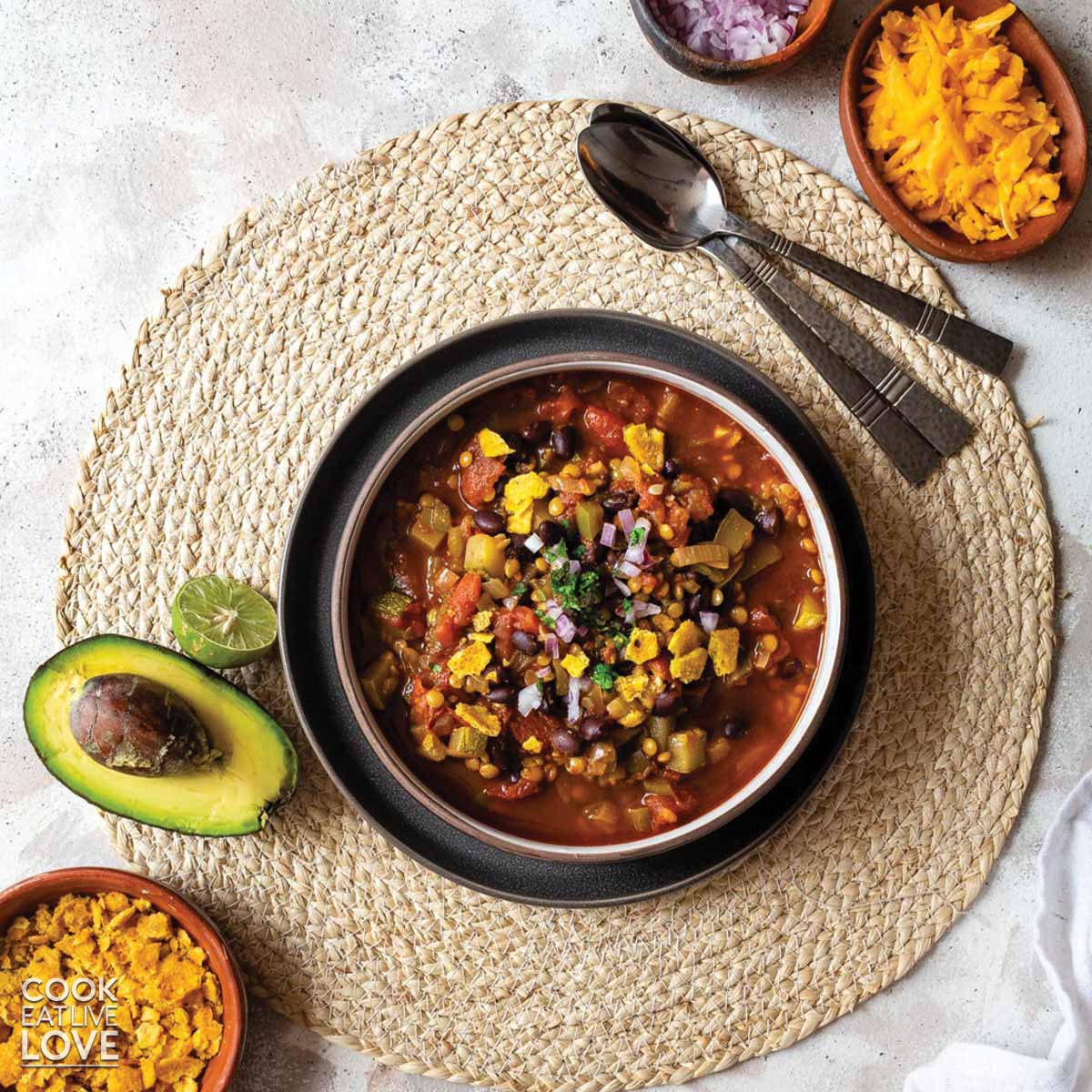 Bowl of bean lentil chili with tomato and avocado and tortilla chips to top it.