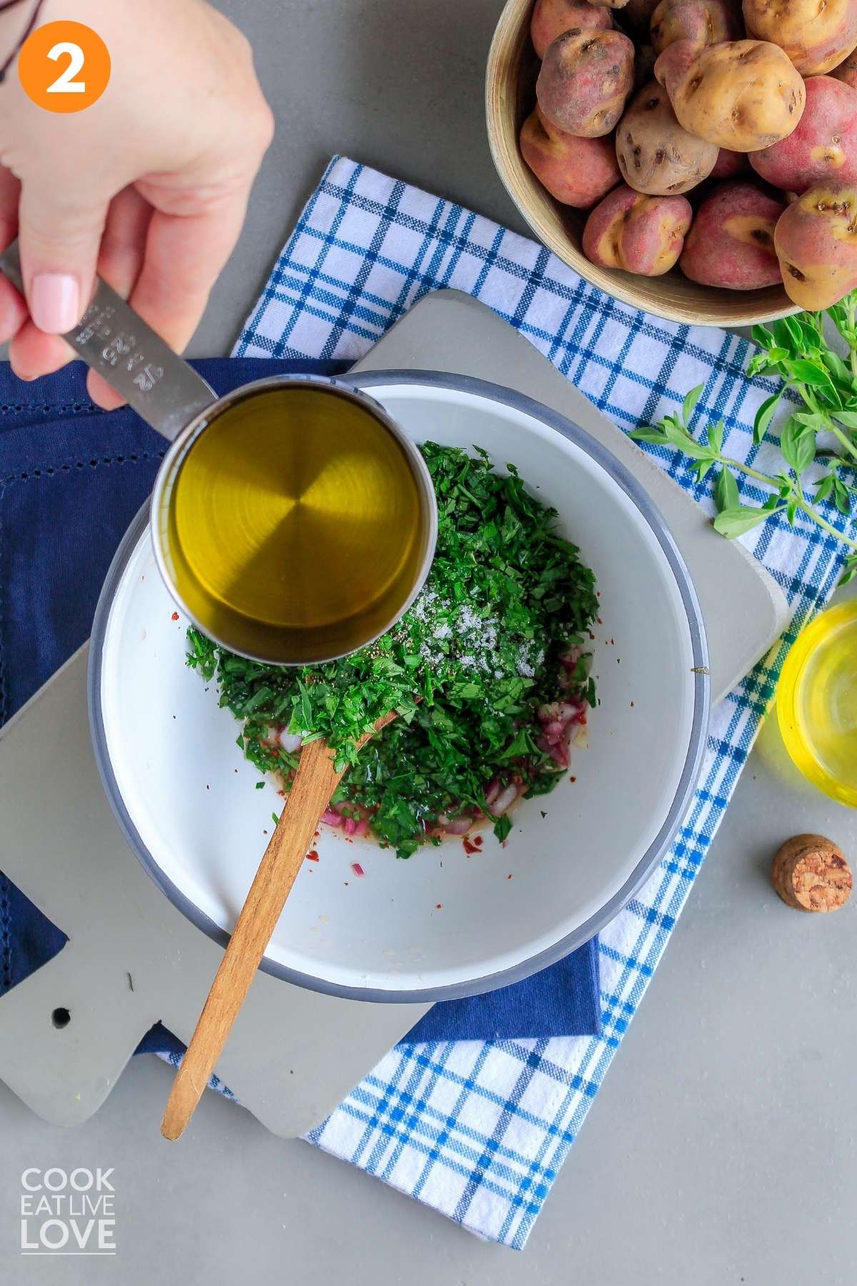 Adding olive oil to the chimichurri ingredients in a bowl.