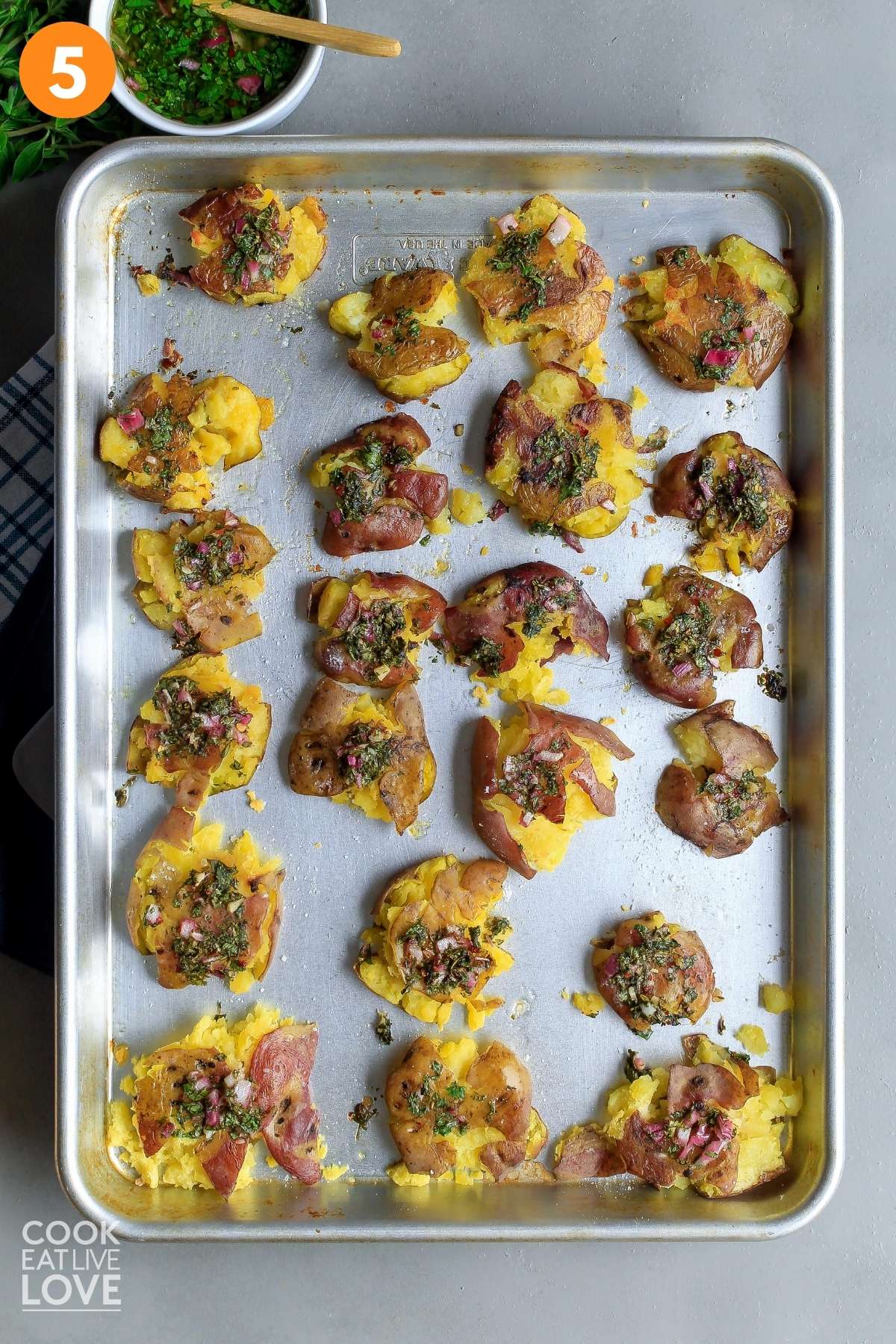 Red smashed potatoes on baking sheet after cooking with chimichurri sauce on top.