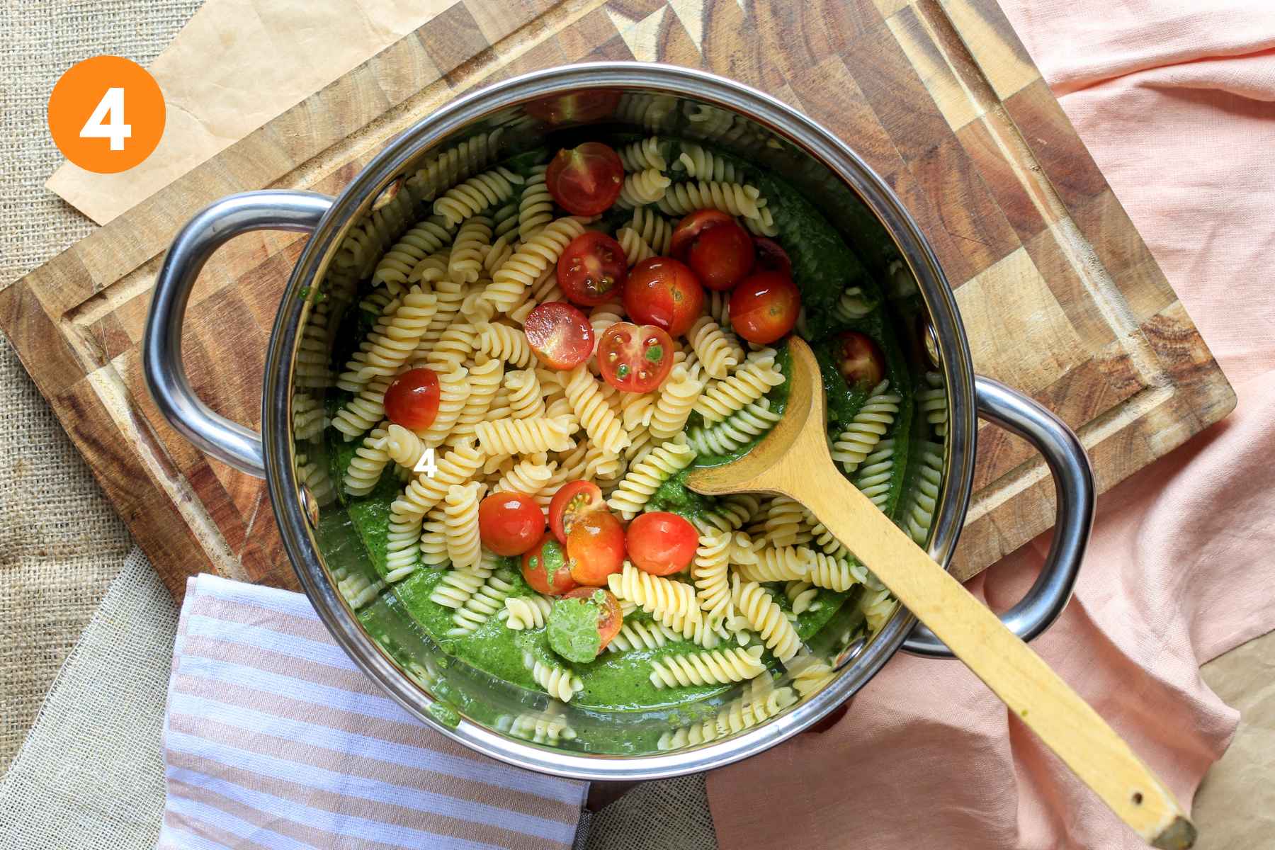 Pasta and tomatoes added to sauce in a pot for spinach pesto pasta.