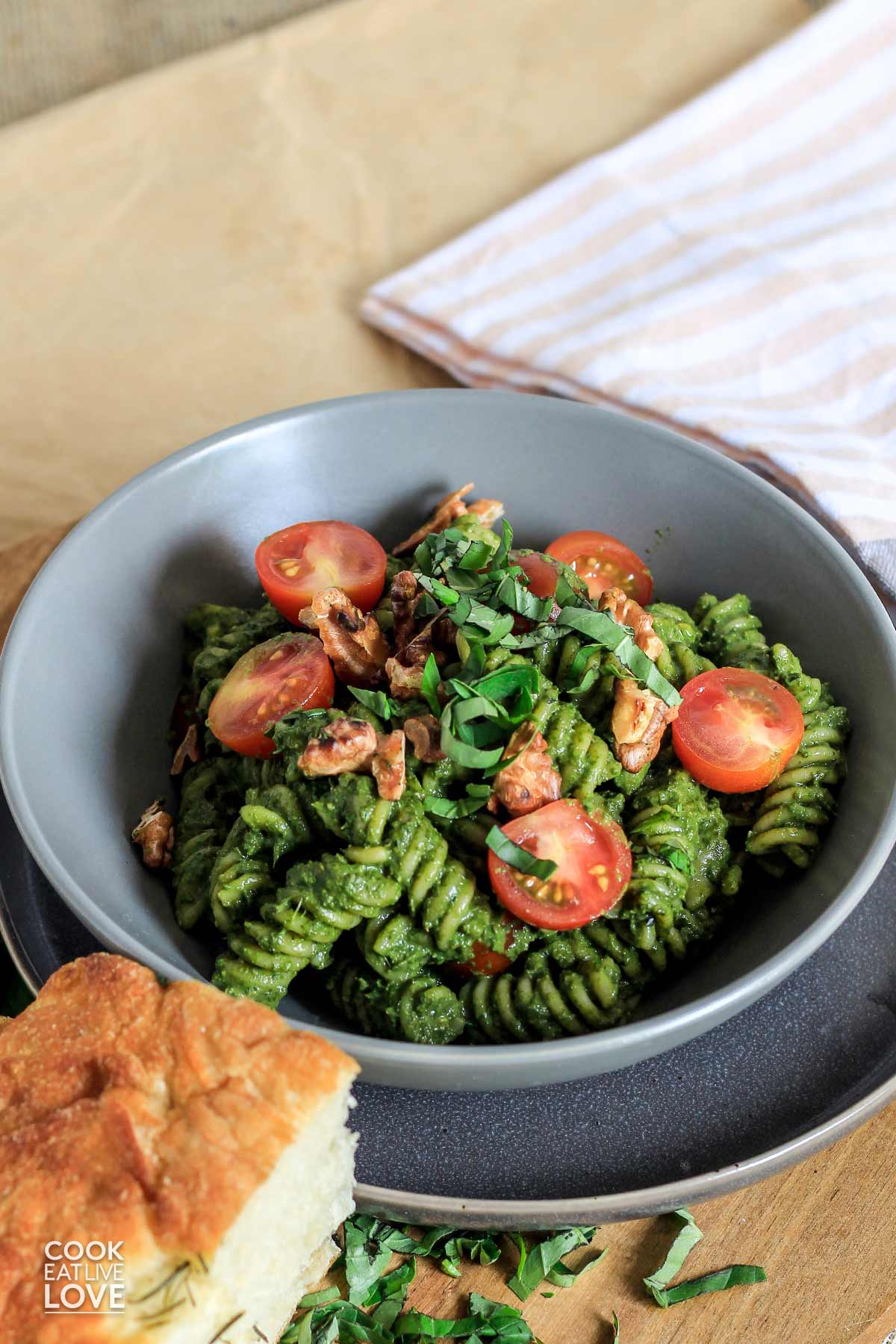 A bowl of spinach pesto pasta on the table with a napkin and piece of bread on the side.