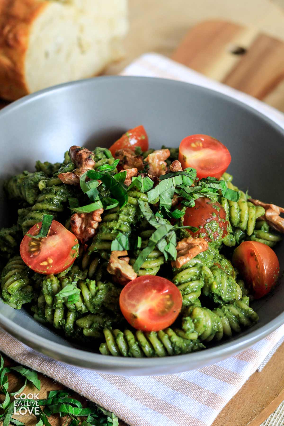 A bowl of vegan spinach pesto pasta topped with tomatoes and walnuts.