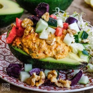 Stuffed avocado on a plate with vegetables over the top.