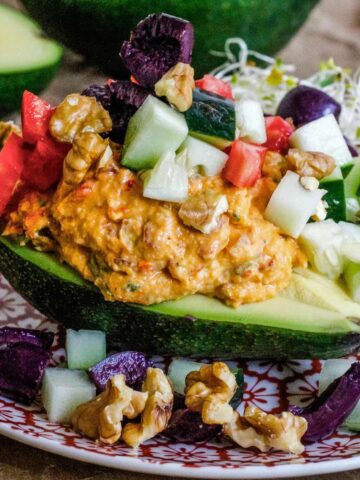 Stuffed avocado on a plate with vegetables over the top.