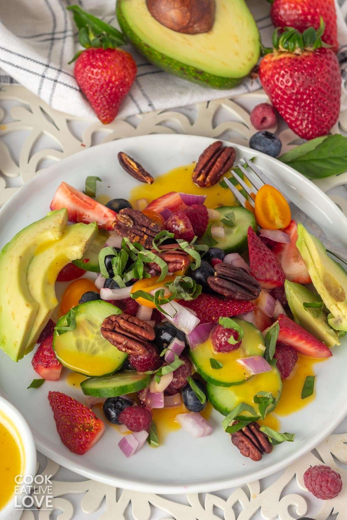 Summer berry salad in a white bowl served on a table with a half an avocado and whole berries.