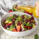 Fresh summer berry salad in a bowl with a bottle of dressing pouring over the top.