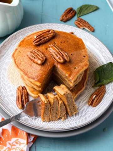 A plate with a stack of sweet potato pancakes with a forkful on the side.