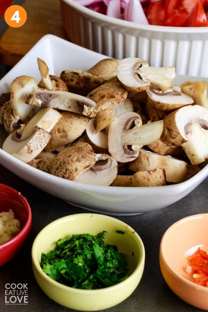 Cut mushrooms in a large bowl and other smaller bowls of ingredients around it.