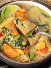 Tofu thai green curry in a bowl on the table with a spoon lifting up a bite.