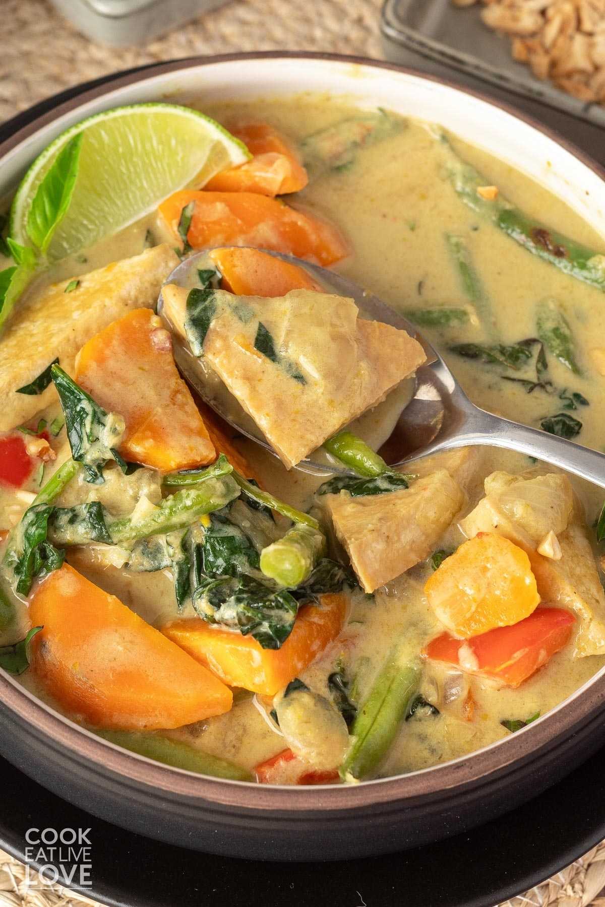 Tofu thai green curry in a bowl on the table with a spoon lifting up a bite. 