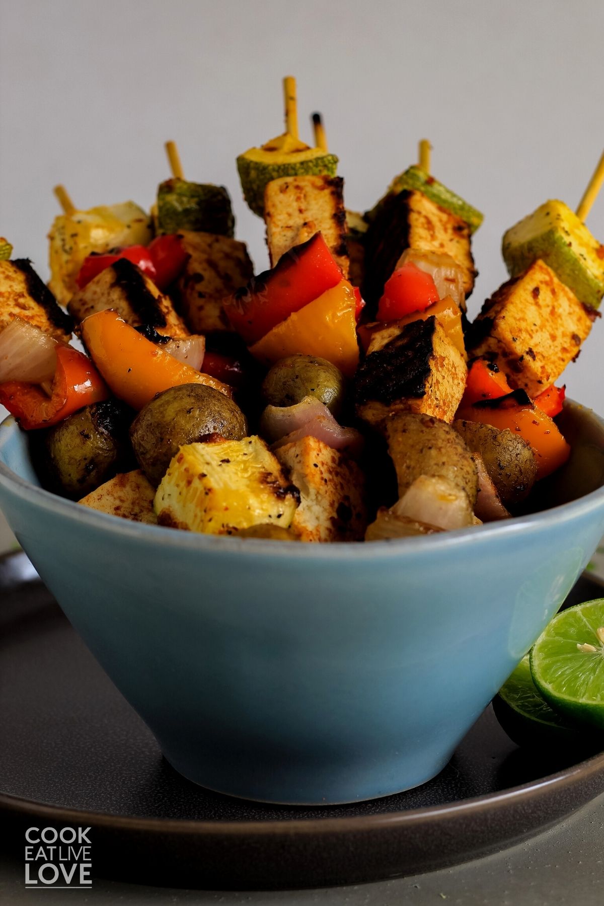 Grilled tofu skewers in a bowl on a plate with a lime half.