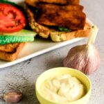 Vegan Roasted garlic aioli in small bowl with a sandwich behind it.