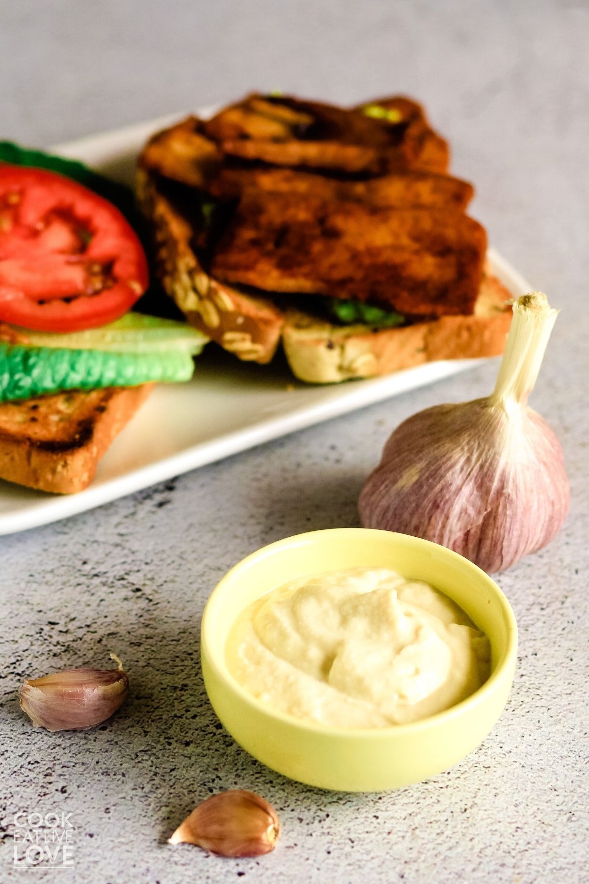 Vegan garlic aioli in a small bowl with a sandwich behind it.