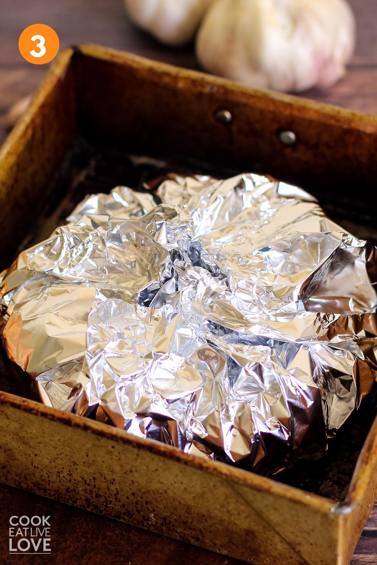 Foil is wrapped up around garlic in a baking pan.