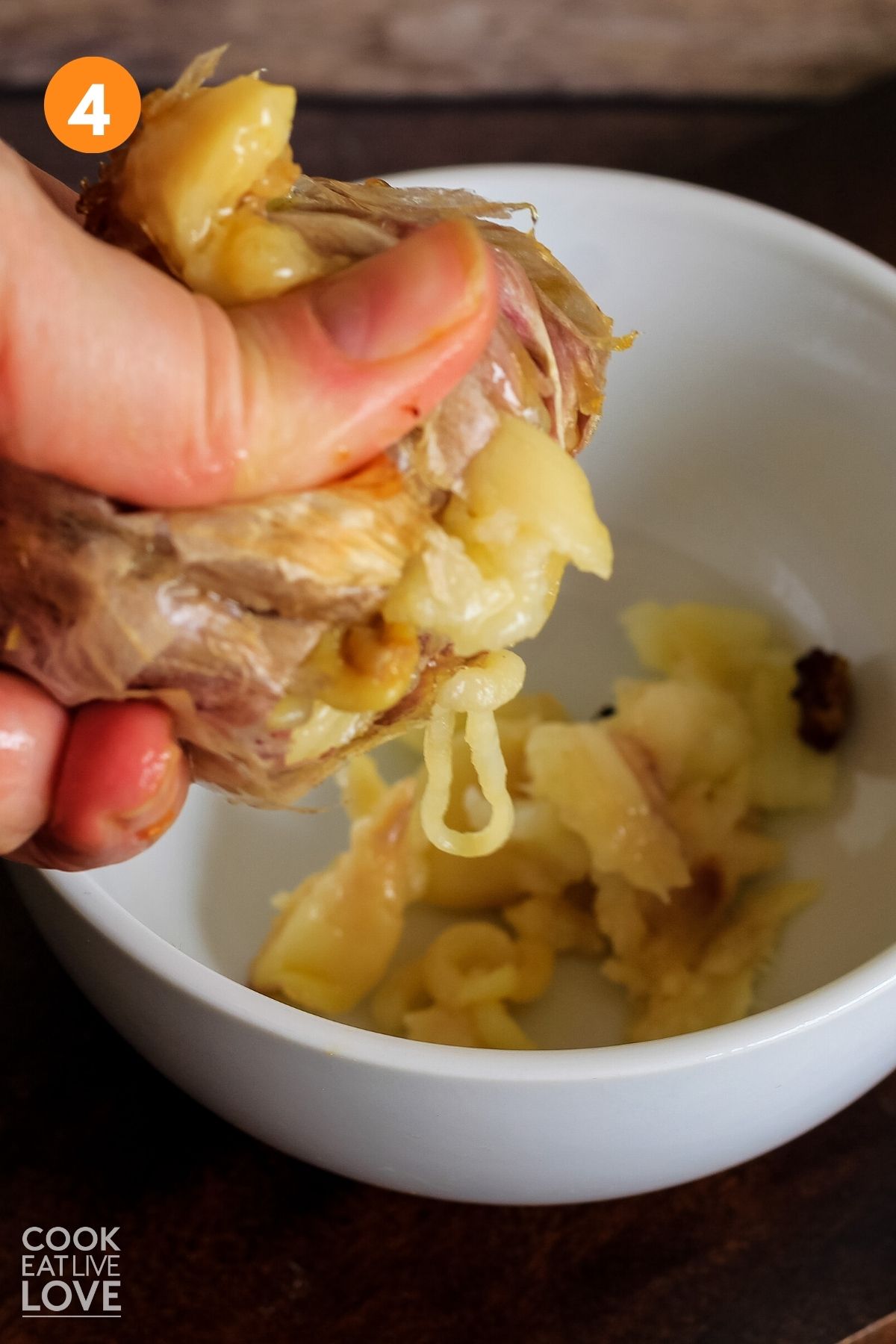 Hand is squeezing roasted garlic from the cooked head.