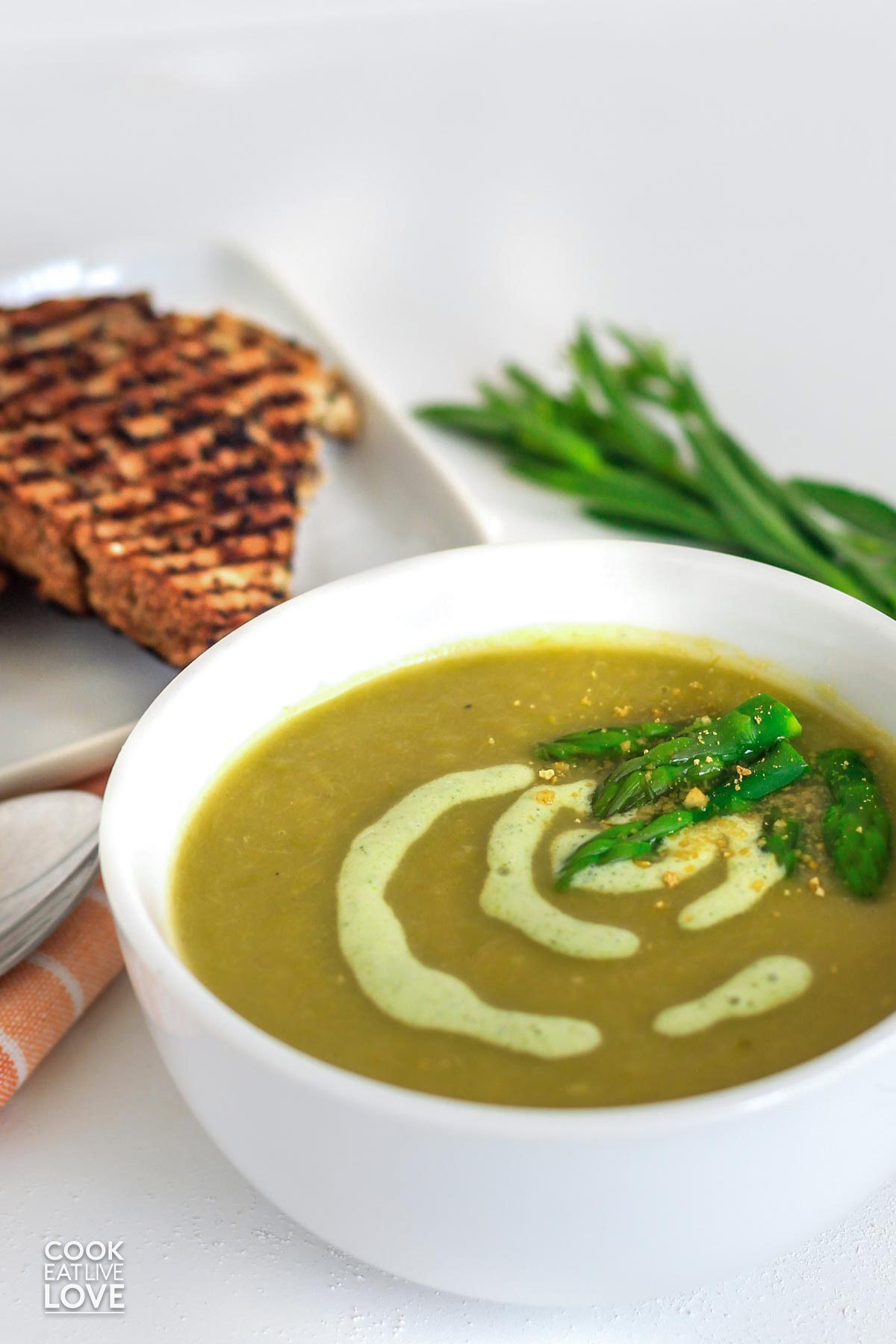 Bowl of vegan cream of asparagus soup with grilled bread on a table.