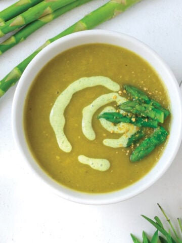 A bowl of vegan asparagus soup in a bowl with asparagus tips.