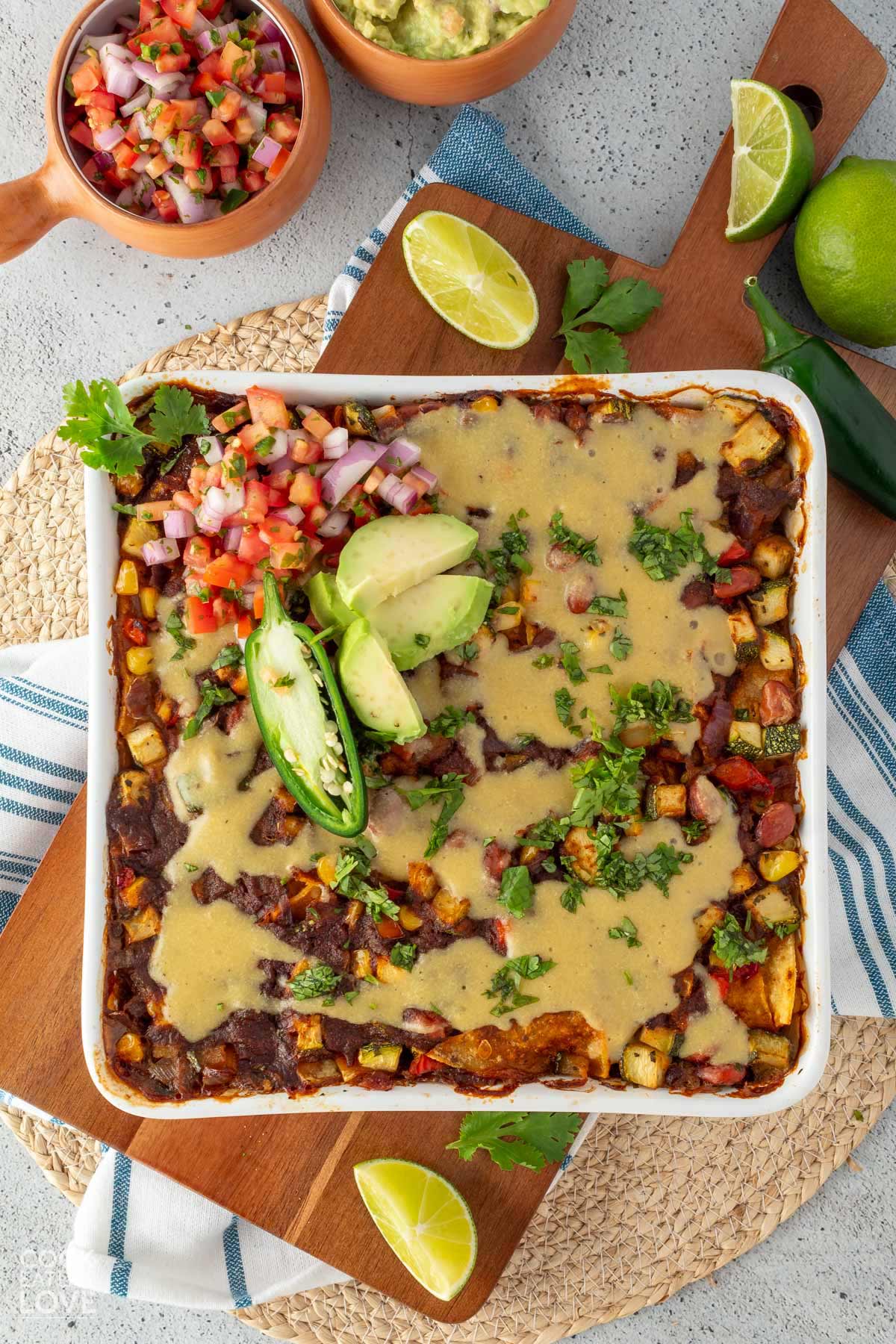Vegan enchilada casserole in a white casserole dish and the top is garnished with avocado, jalapeno, and pico de gallo.