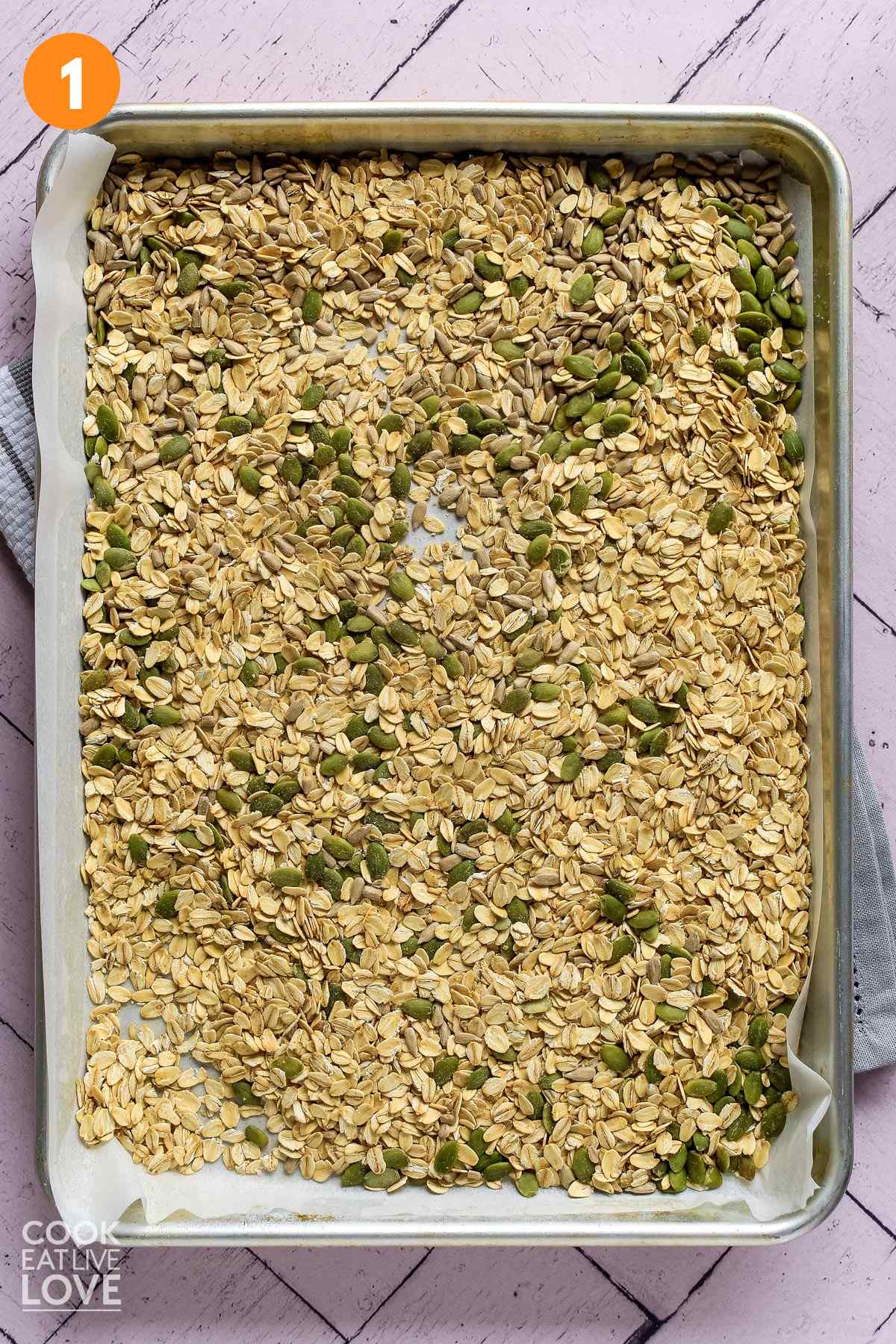 Oats, seeds and almonds on baking sheet ready to toast in the oven.
