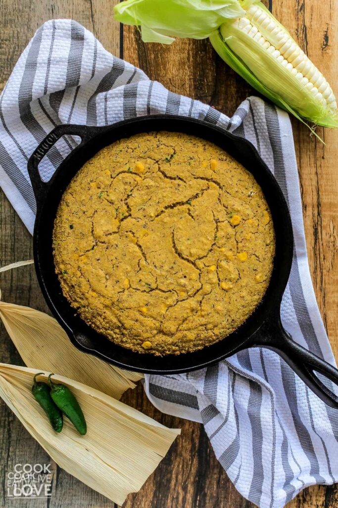 Cooked cornbread in skillet with corn husks and the jalapenos to the side.