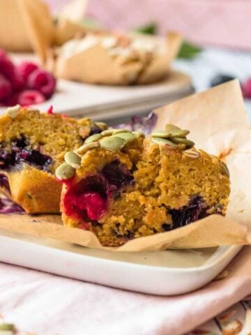 Vegan pumpkin muffins cut in half on a plate on top of parchment paper.