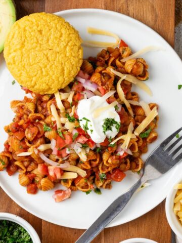 Vegetarian chili mac on a plate with a corn muffin and topped with sour cream.