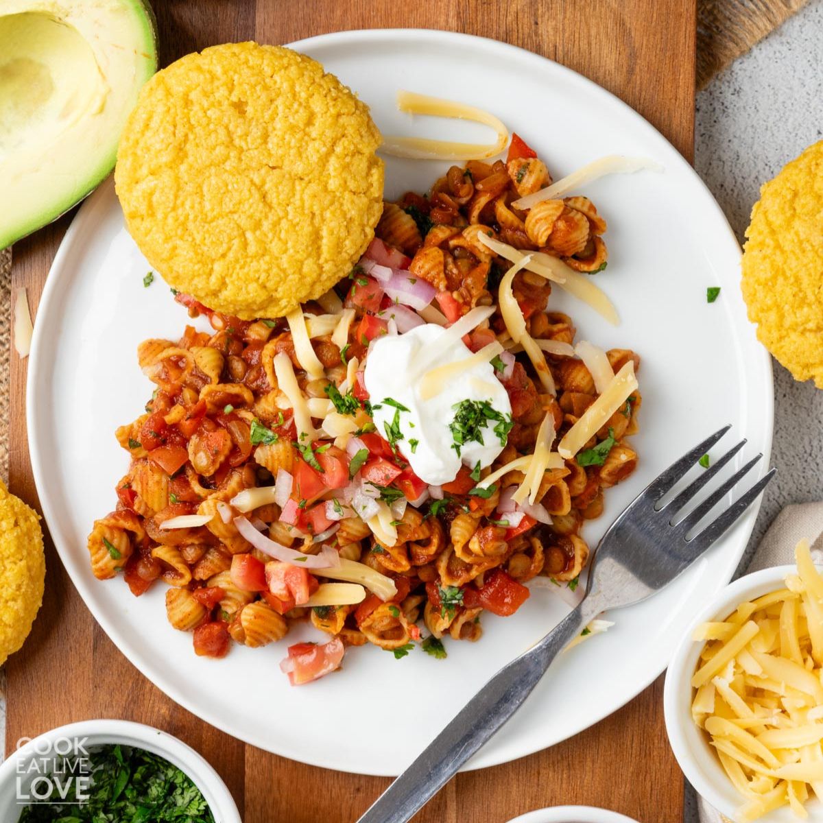 Vegetarian chili mac on a plate with a corn muffin and topped with sour cream.