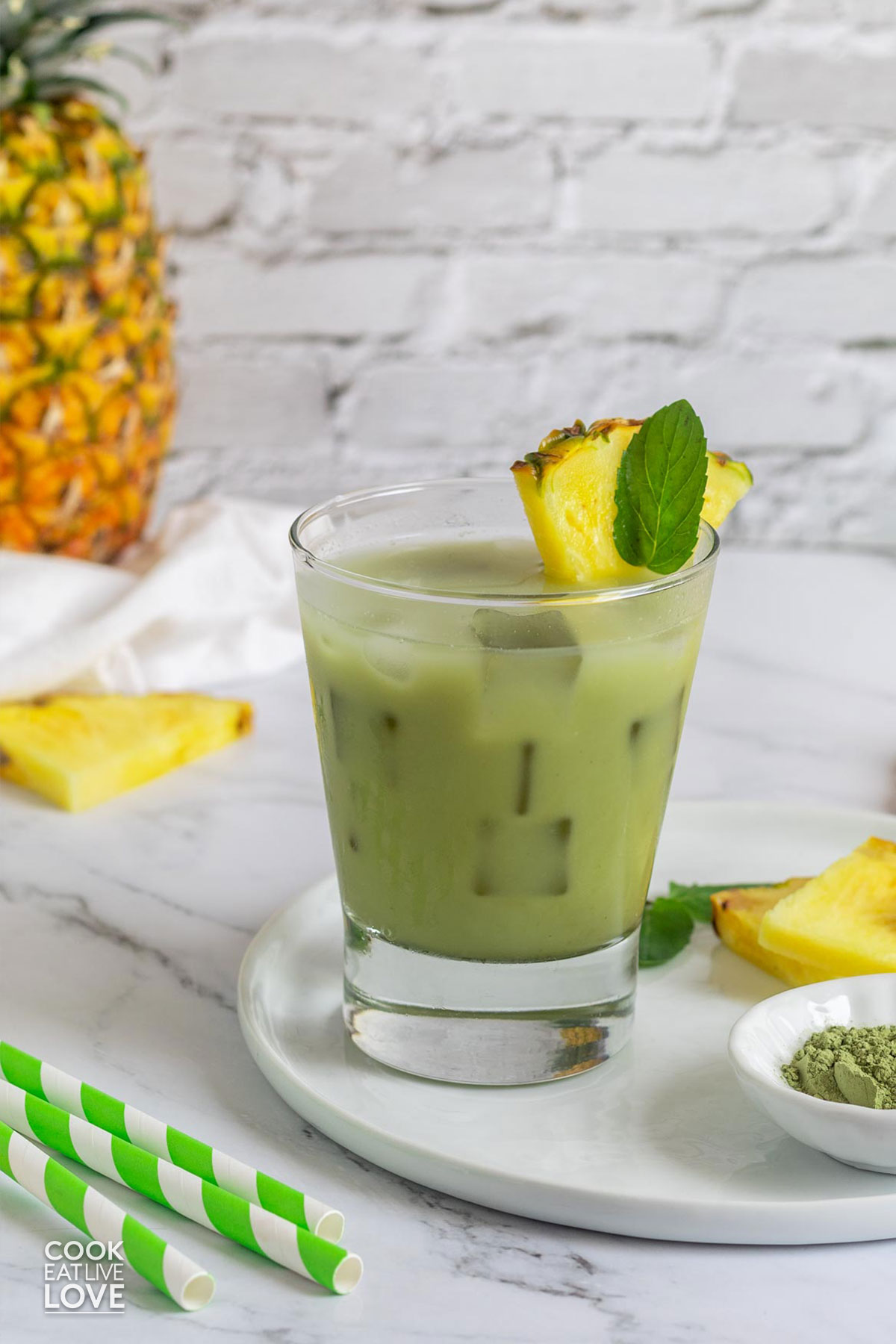 A glass of pineapple matcha drink on the table garnished with fresh mint and pineapple wedge.