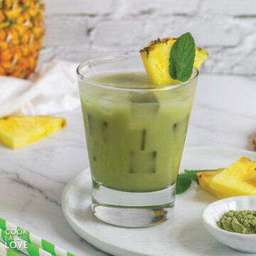 A glass of pineapple matcha drink on the table with a bowl of matcha and pineapple slices.
