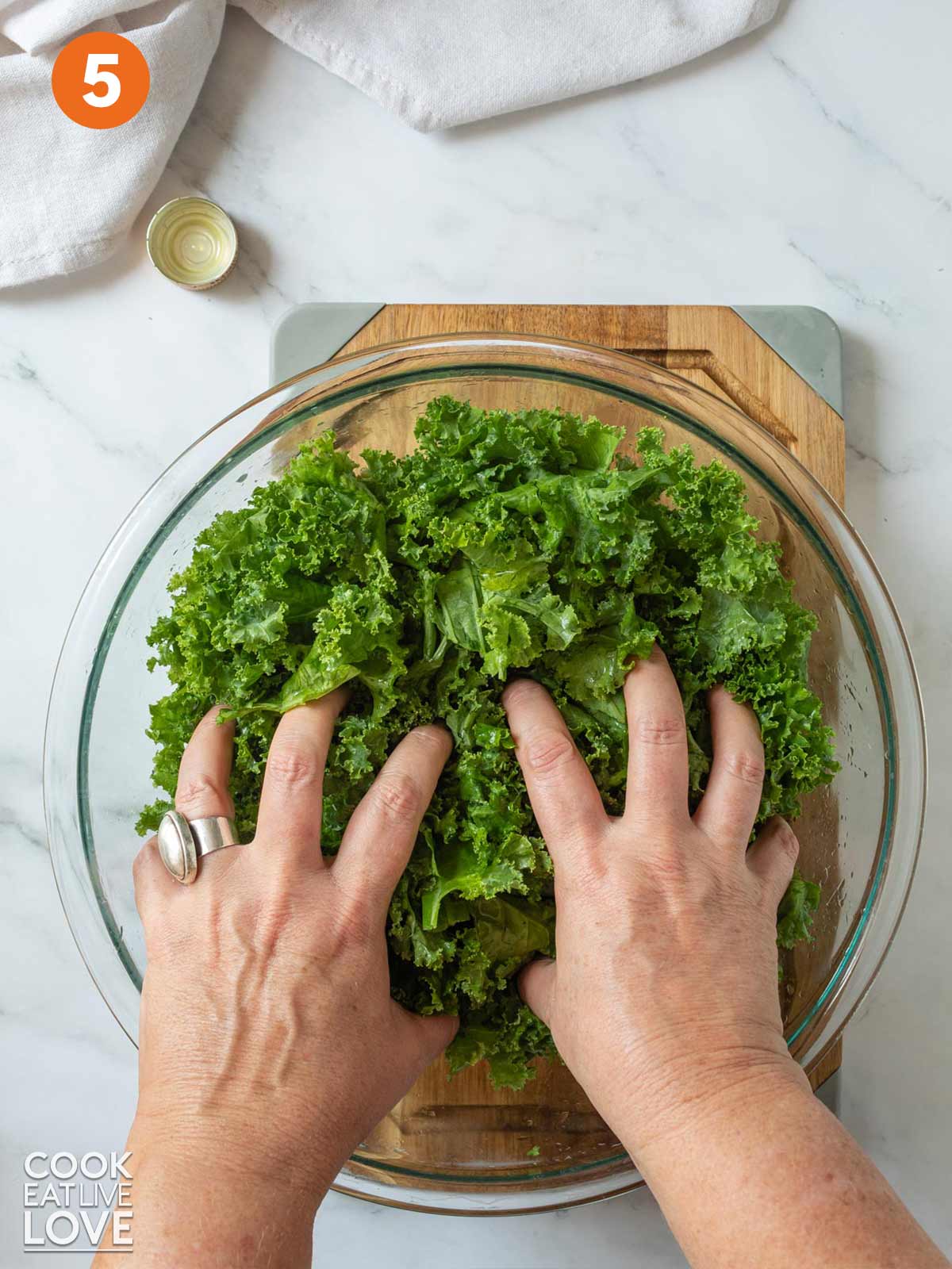 Kale in a bowl with hands massing the oil into the leaves.