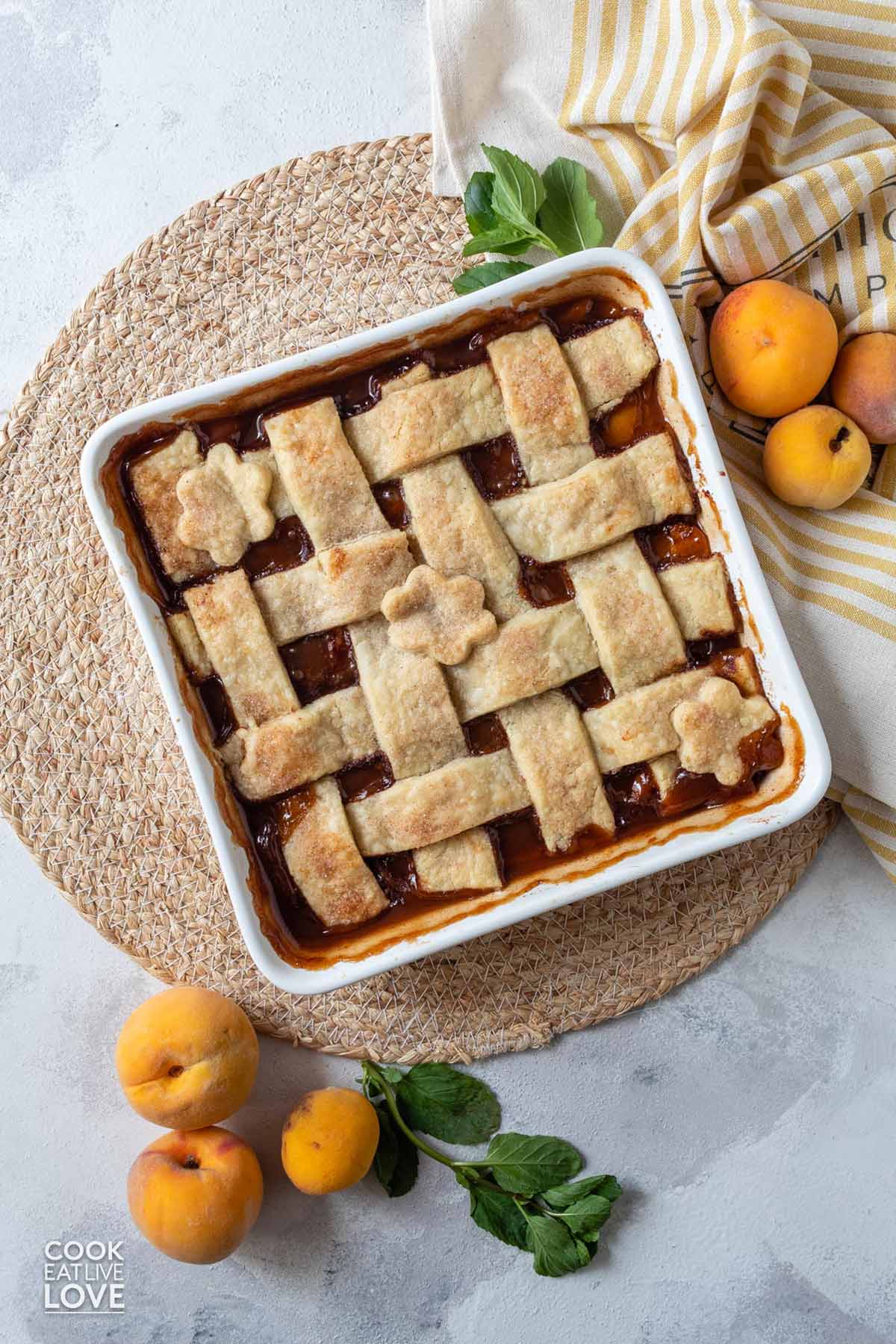 Baked vegan peach cobbler on the table with whole peaches to the side.